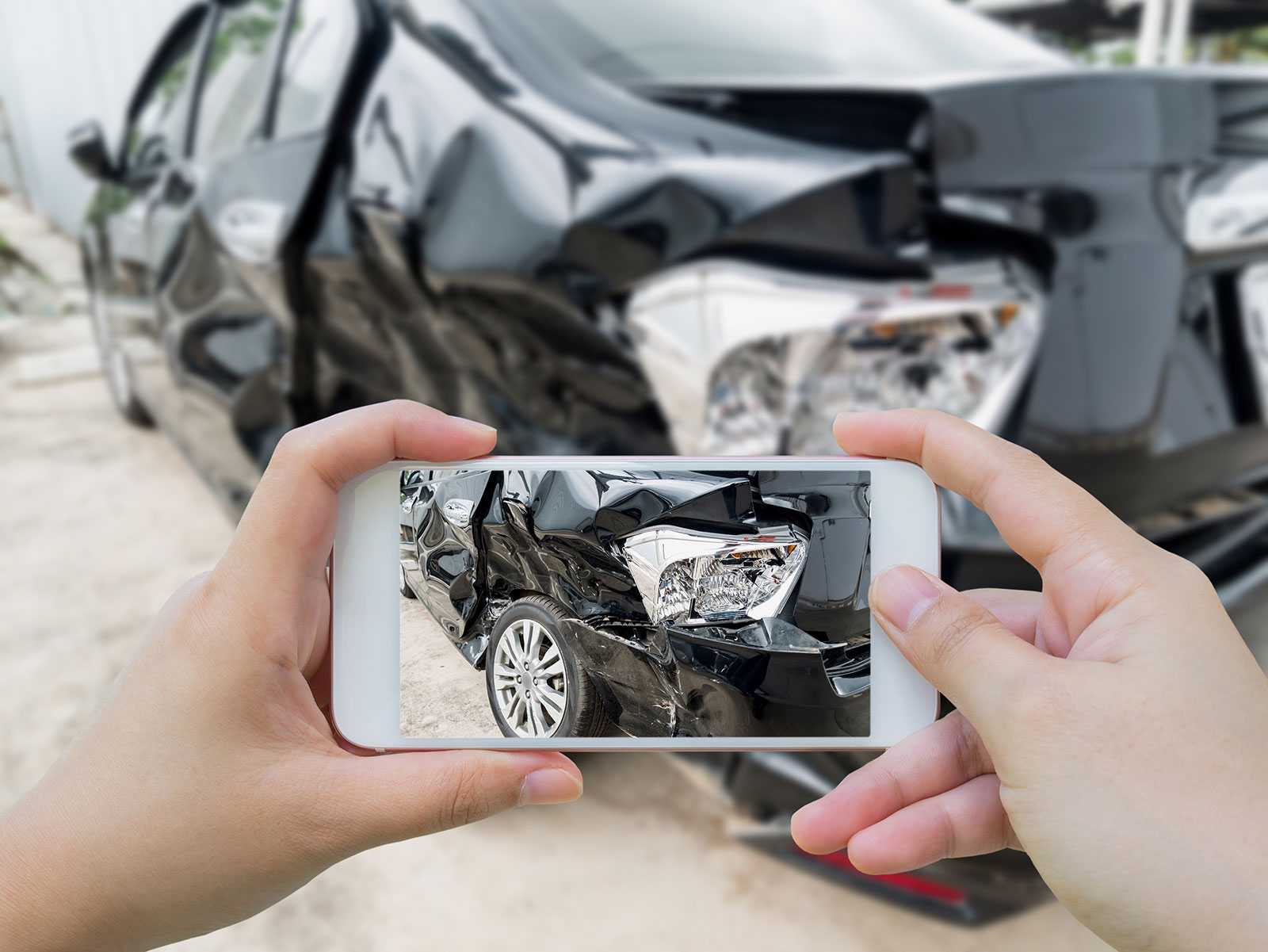 Car accident victim taking a photo of the damage to their black car with their cellphone camera