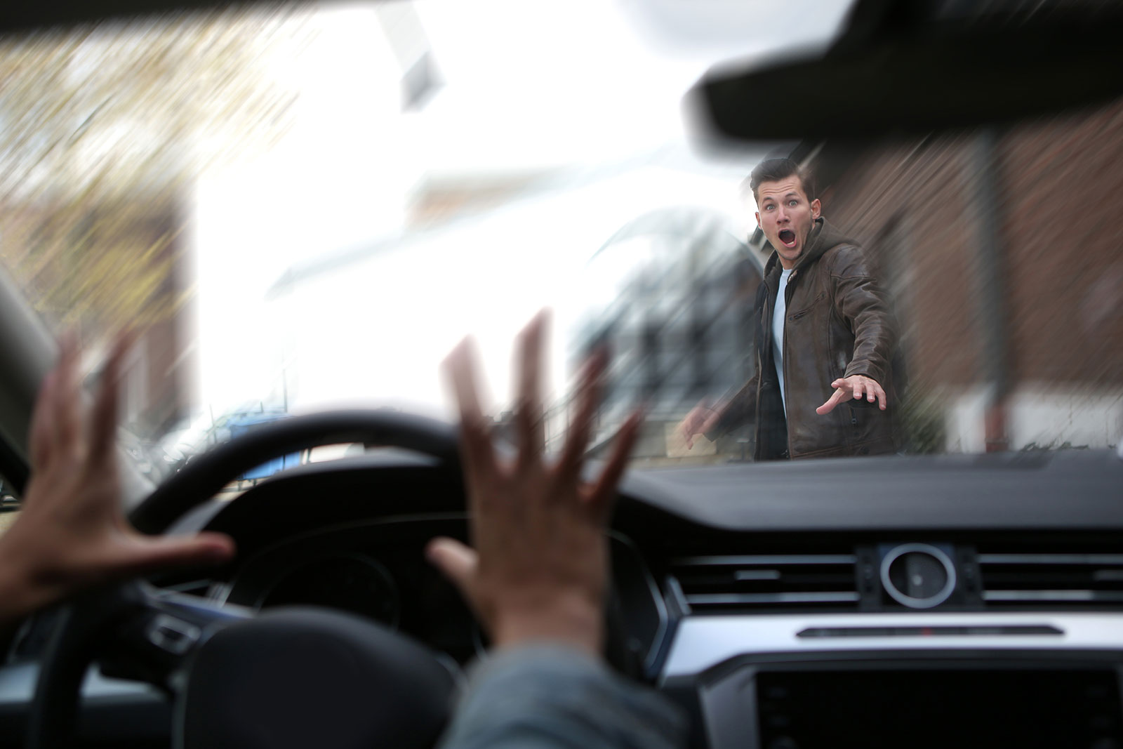 Pedestrian walking across crosswalk with look of fear as car is about to hit him