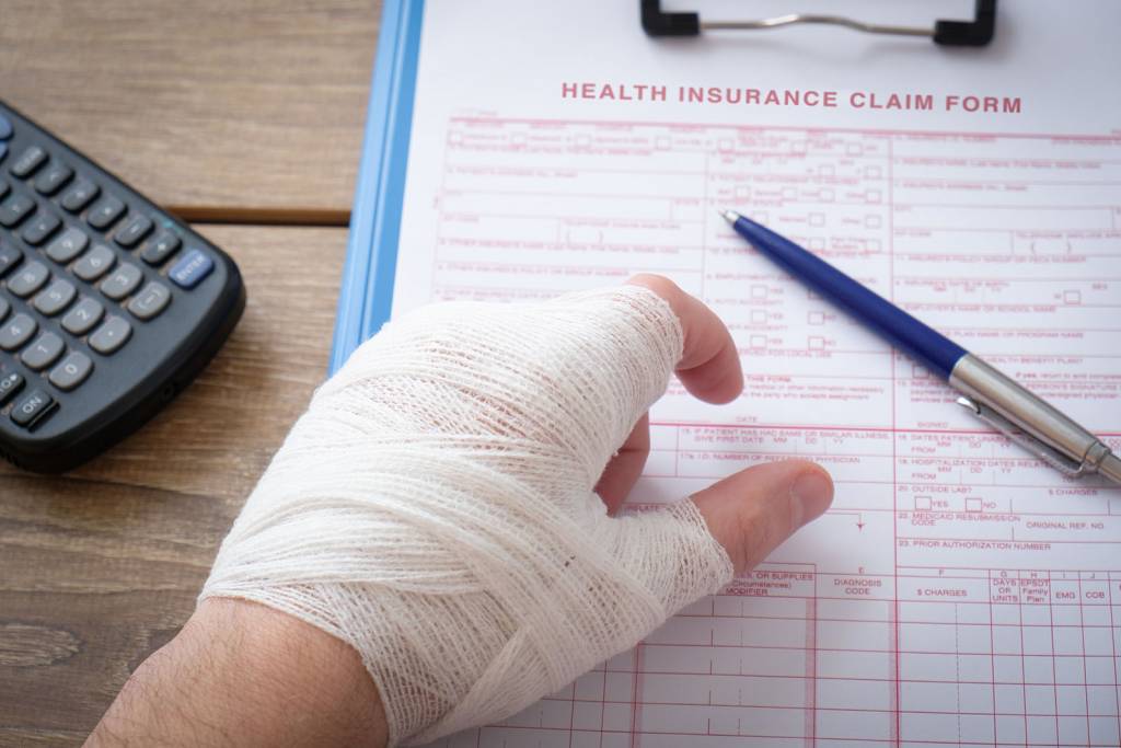 Injured hand wrapped in gauze filling out an injury claim form